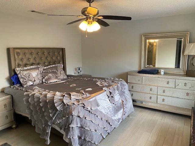 bedroom with a textured ceiling, light wood-type flooring, and ceiling fan