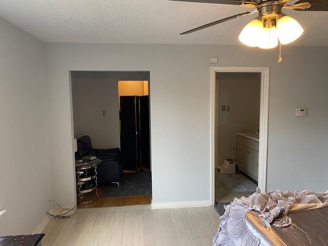 bedroom with a textured ceiling, ensuite bathroom, light wood-type flooring, and ceiling fan