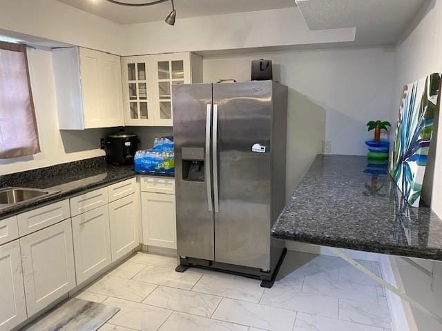 kitchen featuring sink, stainless steel fridge, white cabinetry, and dark stone countertops