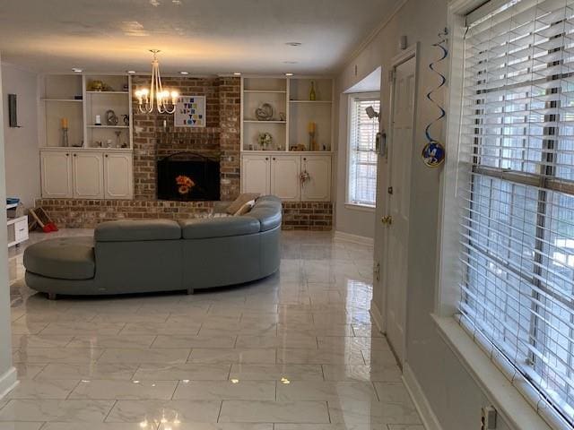 living room featuring a notable chandelier, built in shelves, crown molding, and a brick fireplace