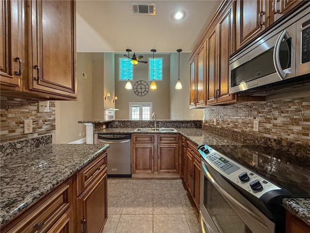 kitchen featuring kitchen peninsula, dark stone counters, stainless steel appliances, sink, and pendant lighting