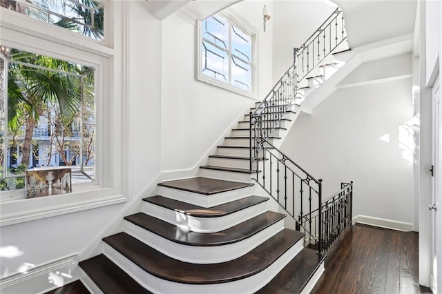 stairway featuring a towering ceiling, wood-type flooring, and plenty of natural light