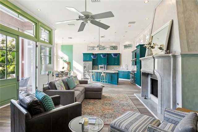 living room featuring ornamental molding, sink, ceiling fan, and light hardwood / wood-style flooring