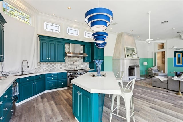 kitchen with high end stainless steel range, blue cabinetry, sink, a large fireplace, and wall chimney exhaust hood