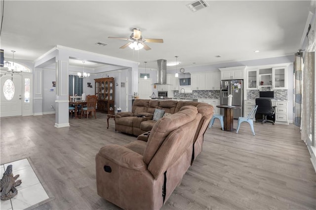 living room with light hardwood / wood-style floors, ornamental molding, and ceiling fan with notable chandelier