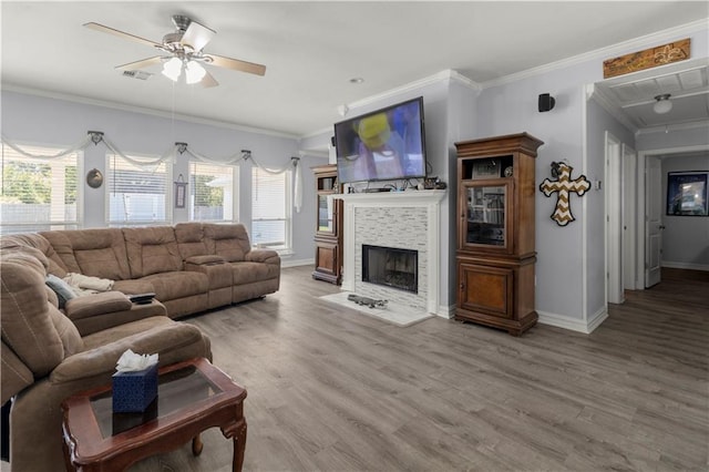 living room with ornamental molding, hardwood / wood-style floors, a stone fireplace, and ceiling fan