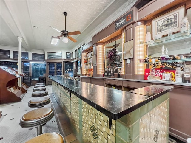 bar featuring ceiling fan, crown molding, decorative columns, and a textured ceiling