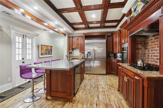 kitchen with appliances with stainless steel finishes, sink, light wood-type flooring, ornamental molding, and a center island with sink