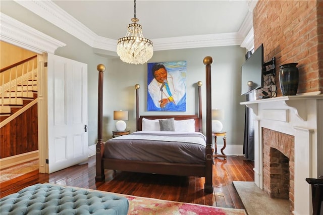 bedroom featuring ornamental molding, a notable chandelier, wood-type flooring, and a large fireplace