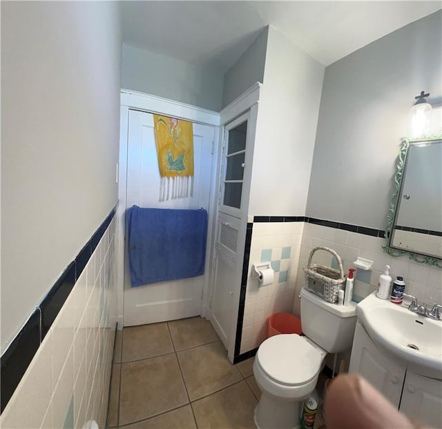 bathroom featuring wainscoting, tile patterned flooring, vanity, toilet, and tile walls