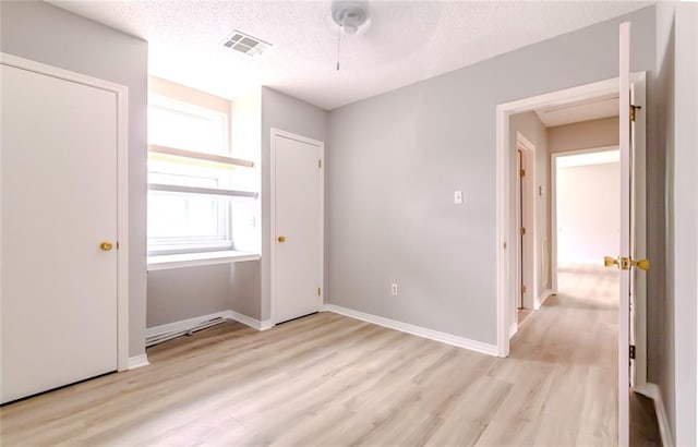 unfurnished bedroom featuring ceiling fan, light wood-type flooring, and a textured ceiling