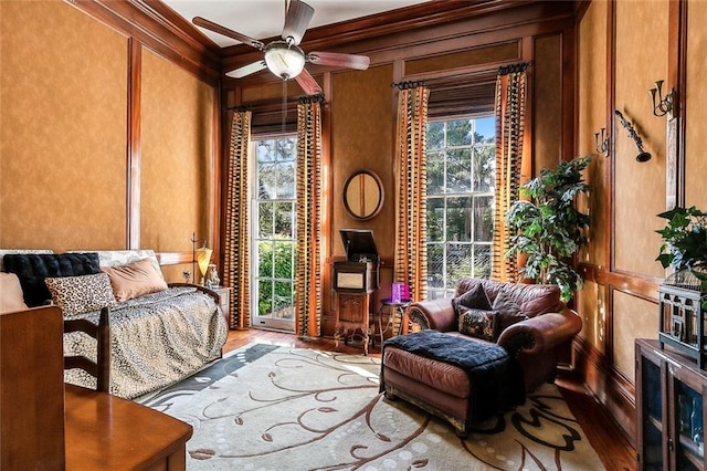 living area with crown molding, wood-type flooring, and ceiling fan