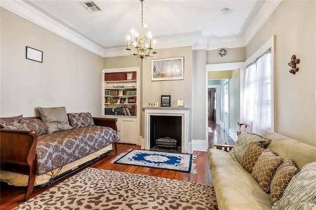 living room with ornamental molding, an inviting chandelier, hardwood / wood-style floors, and built in features