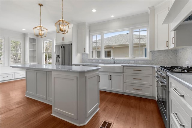 kitchen with stainless steel appliances, wood-type flooring, a center island, white cabinetry, and decorative light fixtures