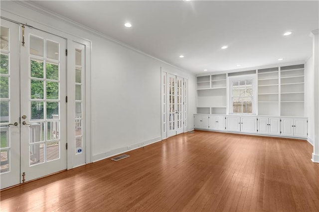 unfurnished living room featuring built in shelves, light wood-type flooring, french doors, and crown molding