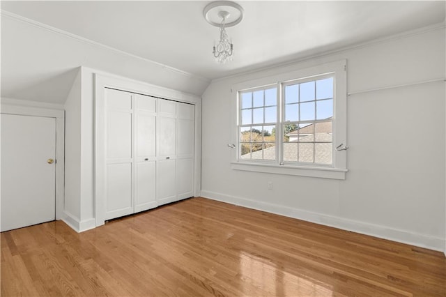 unfurnished bedroom with light hardwood / wood-style floors, crown molding, vaulted ceiling, and a closet