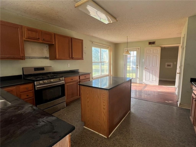 kitchen featuring stainless steel gas stove, a center island, decorative light fixtures, and a textured ceiling