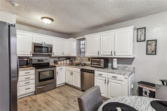 kitchen featuring stainless steel appliances, sink, white cabinets, a textured ceiling, and light hardwood / wood-style floors