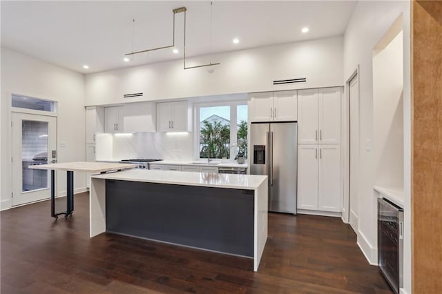 kitchen with high quality fridge, decorative light fixtures, white cabinetry, wine cooler, and backsplash