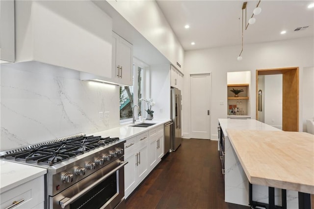 kitchen with sink, dark hardwood / wood-style floors, light stone counters, premium appliances, and white cabinets