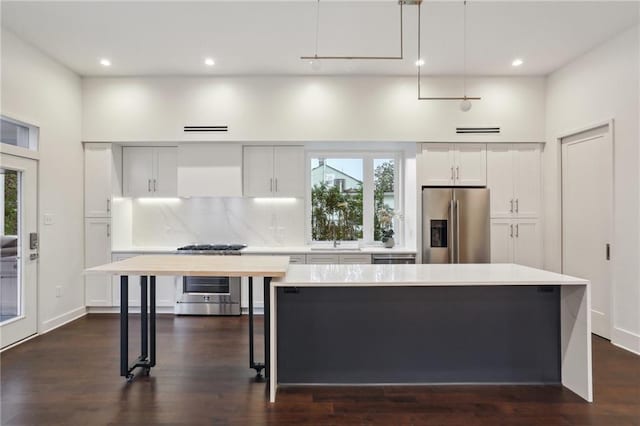 kitchen with pendant lighting, appliances with stainless steel finishes, tasteful backsplash, white cabinets, and a kitchen island