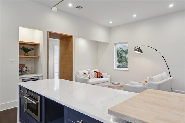 kitchen featuring built in features, light stone countertops, blue cabinets, dark hardwood / wood-style flooring, and oven