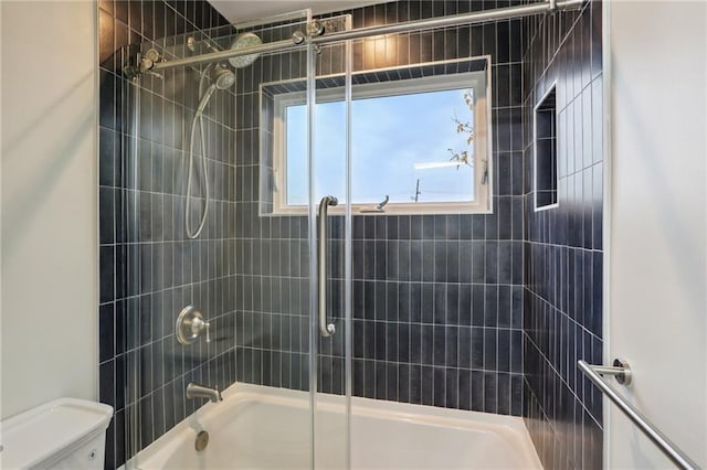 bathroom featuring toilet and bath / shower combo with glass door