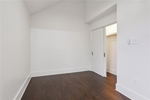 spare room with dark wood-type flooring and lofted ceiling