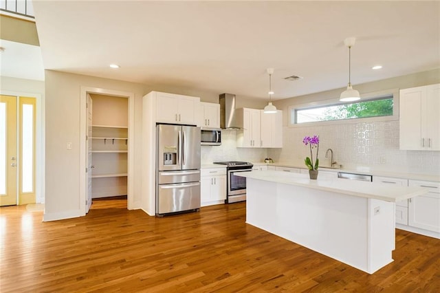 kitchen with wall chimney exhaust hood, white cabinetry, appliances with stainless steel finishes, and pendant lighting