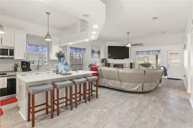 kitchen featuring appliances with stainless steel finishes, a kitchen island, pendant lighting, white cabinets, and a breakfast bar