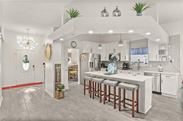 kitchen featuring appliances with stainless steel finishes, white cabinetry, sink, pendant lighting, and a center island