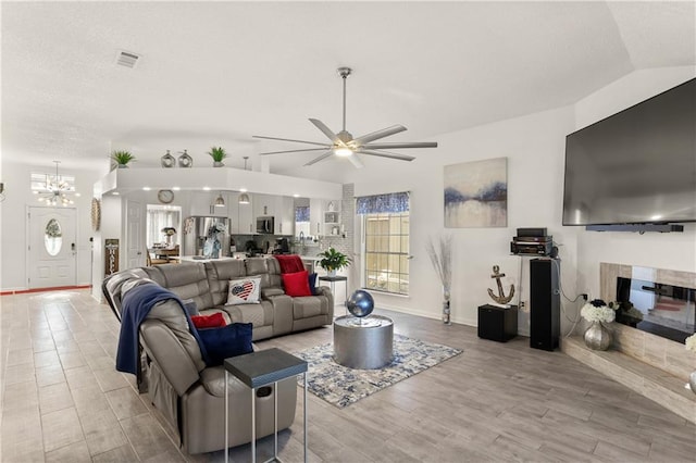 living room with light hardwood / wood-style floors, lofted ceiling, ceiling fan with notable chandelier, and a fireplace