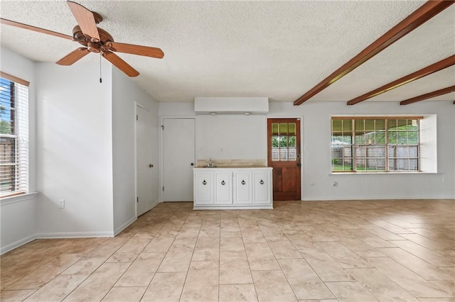 unfurnished living room with a textured ceiling, beamed ceiling, and ceiling fan