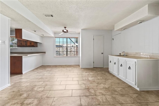 kitchen with sink, a textured ceiling, ceiling fan, white cabinets, and light tile patterned floors