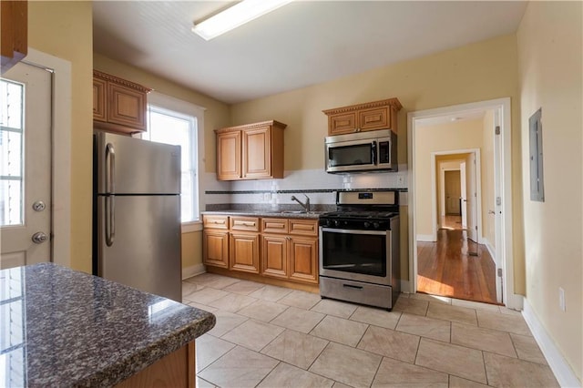 kitchen with sink, dark stone countertops, tasteful backsplash, light tile patterned flooring, and stainless steel appliances