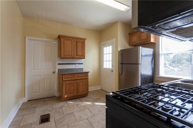 kitchen with black gas range, stainless steel refrigerator, and light tile patterned flooring