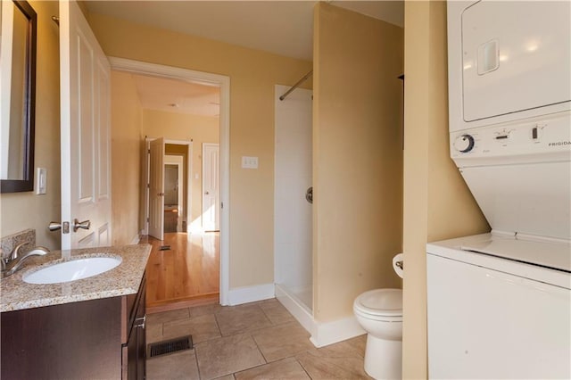 bathroom with tile patterned floors, walk in shower, vanity, stacked washer and clothes dryer, and toilet