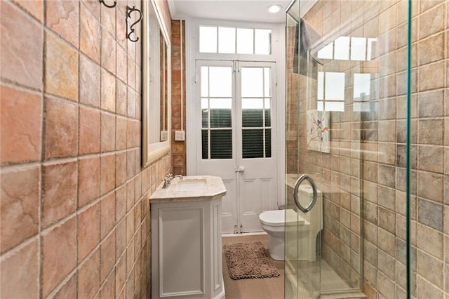 bathroom with toilet, tile patterned floors, walk in shower, tile walls, and vanity