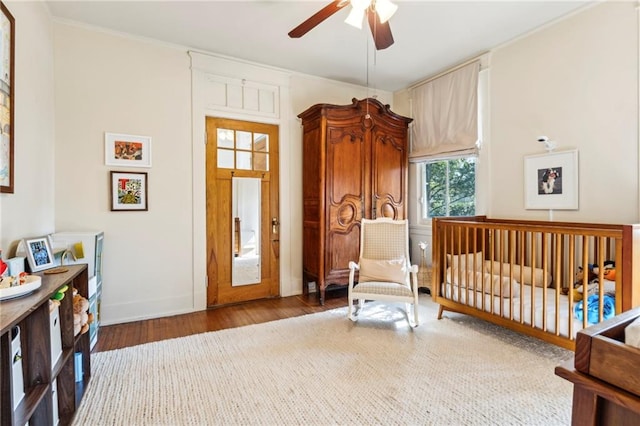 bedroom with ceiling fan, a crib, and hardwood / wood-style floors