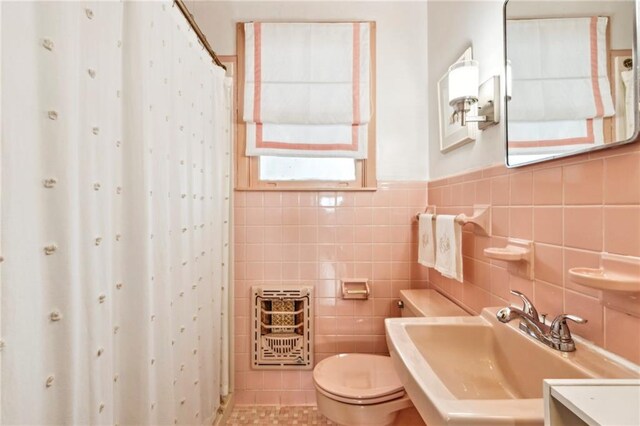 bathroom with heating unit, walk in shower, tile walls, toilet, and sink