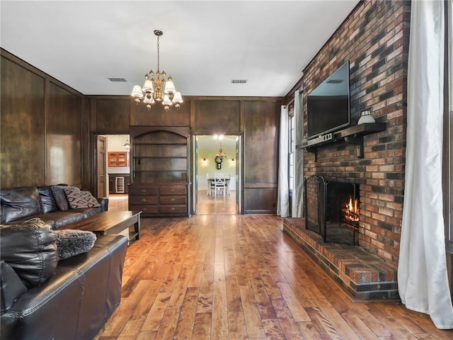 living room with a brick fireplace, an inviting chandelier, light hardwood / wood-style flooring, and wood walls