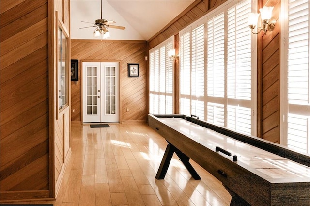 playroom featuring wood walls, light wood-type flooring, french doors, ceiling fan, and high vaulted ceiling