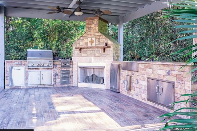 view of patio featuring an outdoor stone fireplace, grilling area, ceiling fan, a deck, and an outdoor kitchen