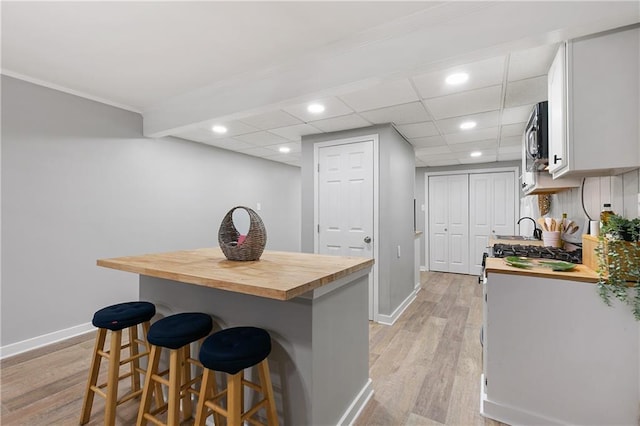 kitchen with a drop ceiling, butcher block counters, a kitchen breakfast bar, decorative backsplash, and light hardwood / wood-style flooring