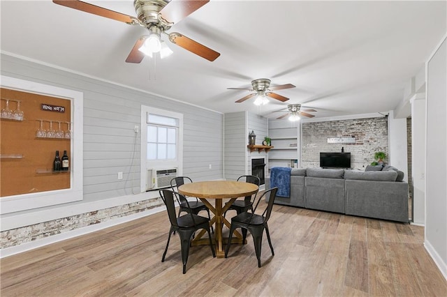 dining area featuring a fireplace, wooden walls, light wood-type flooring, and ceiling fan