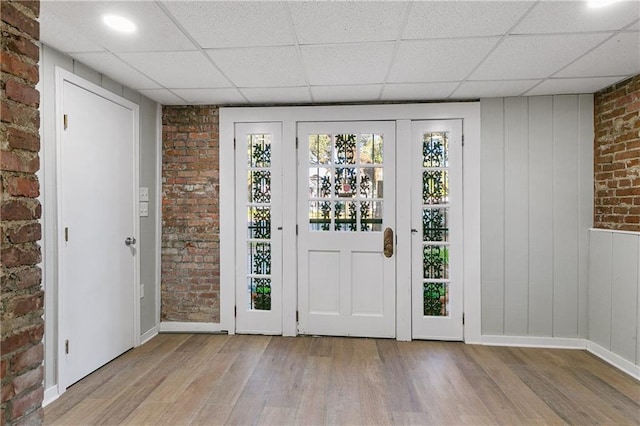 doorway to outside with brick wall, a drop ceiling, and light wood-type flooring