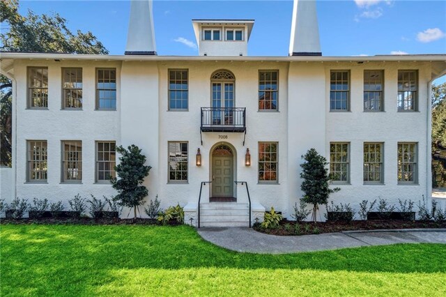 view of front of property with stucco siding, a balcony, and a front lawn