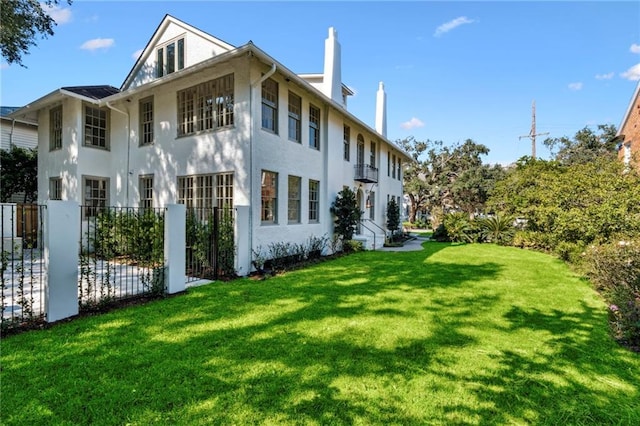 rear view of property with stucco siding, fence, a chimney, and a yard