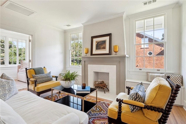 living room with attic access, visible vents, ornamental molding, and light wood-style floors