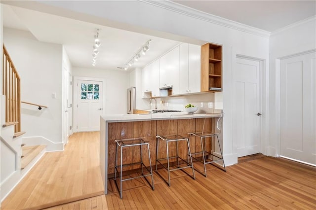 kitchen with white cabinets, a kitchen bar, light wood finished floors, and a peninsula